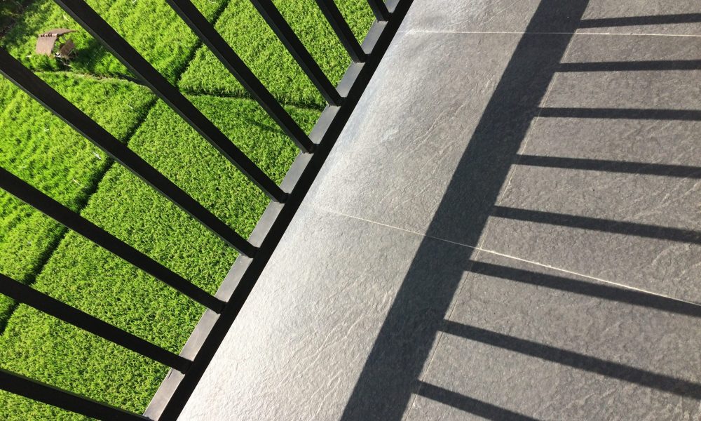 A metal fence shadow on the balcony with a view of a grassy field on a sunny day
