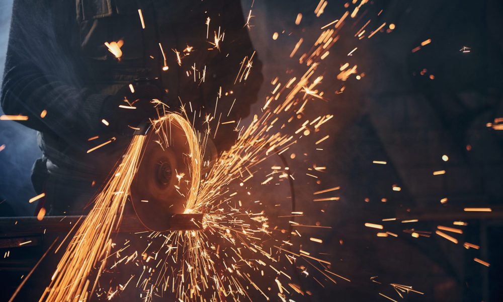 Close up of worker cutting metal pipe with large yellow sparks. Concept of working with angle grinder and polishing or welding metal in factory.
